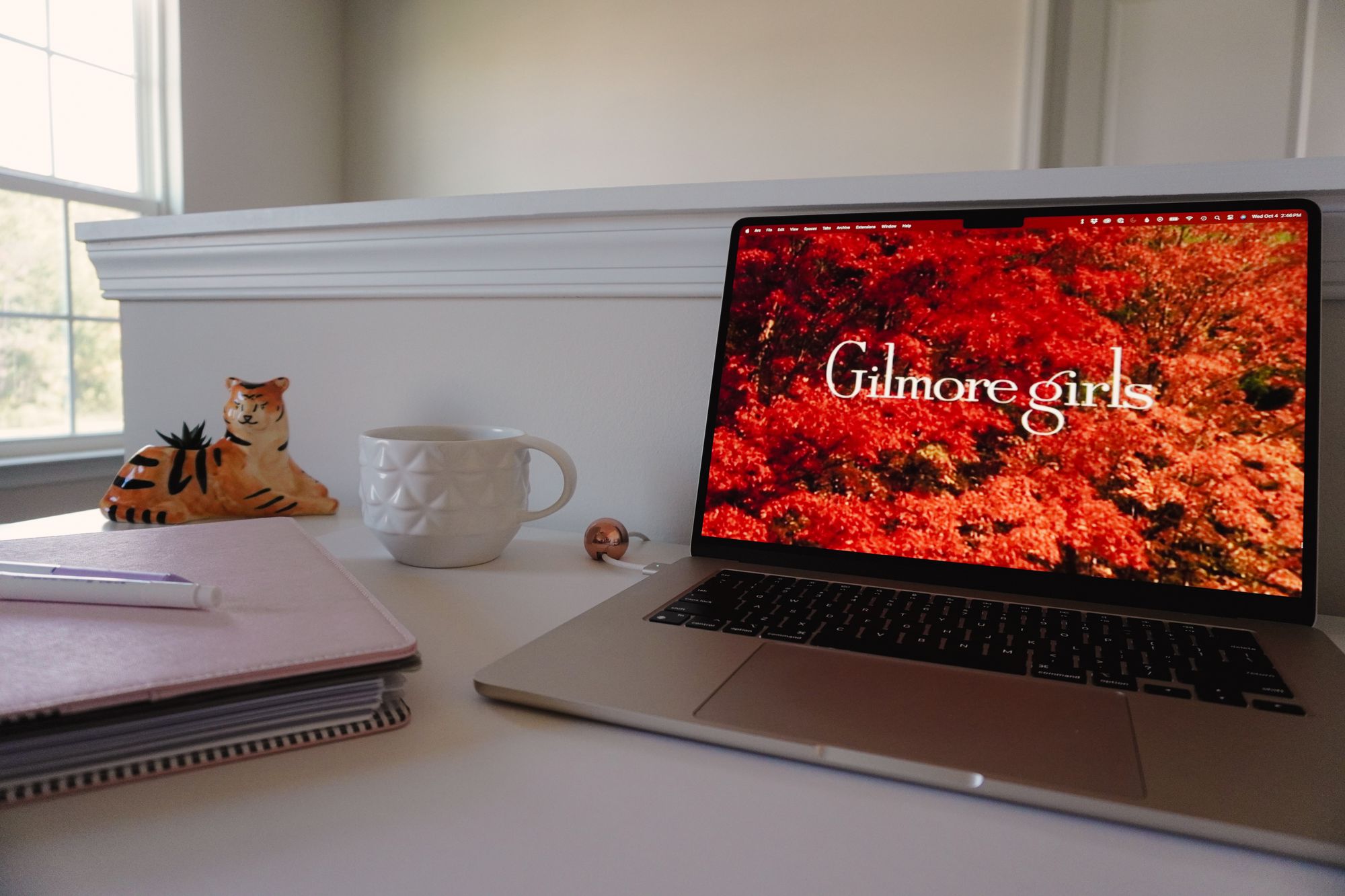 white desk with pink planner, succulent in a tiger-shaped planter, white mug, and MacBook Air showing the Gilmore Girls title screen