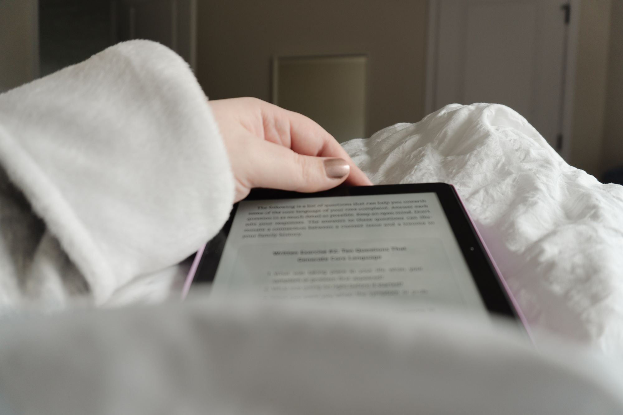 view from bed of a woman's left arm, shown in a cozy robe and wrapped around the top of a Kindle